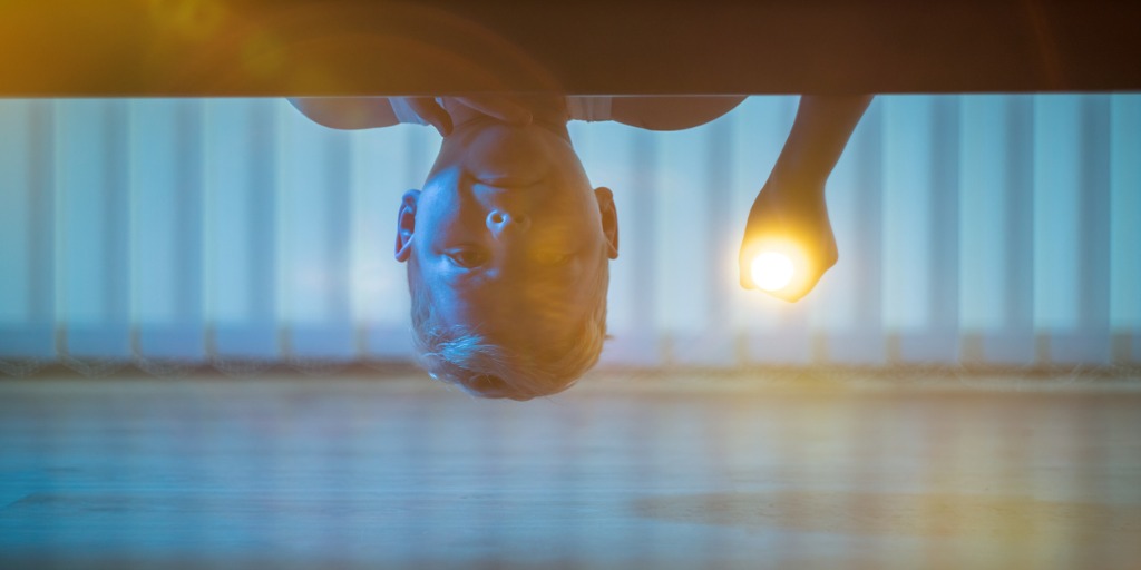 Boy looking under bed with flashlight