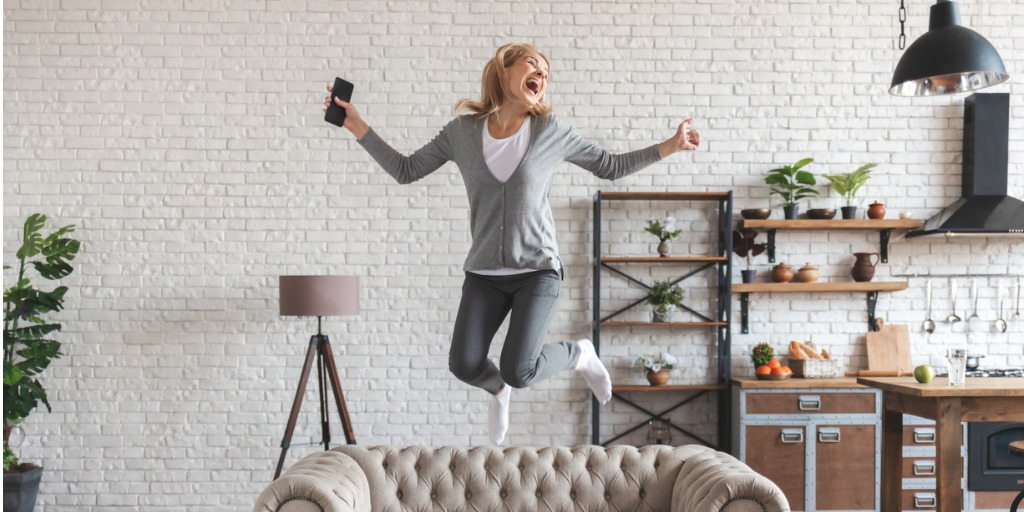 Young woman jumping for joy on sofa after hearing great