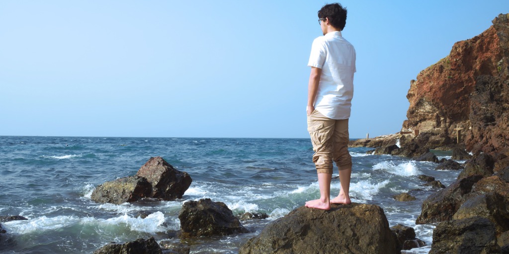 back view of a traveler standing on a rock of seashore 