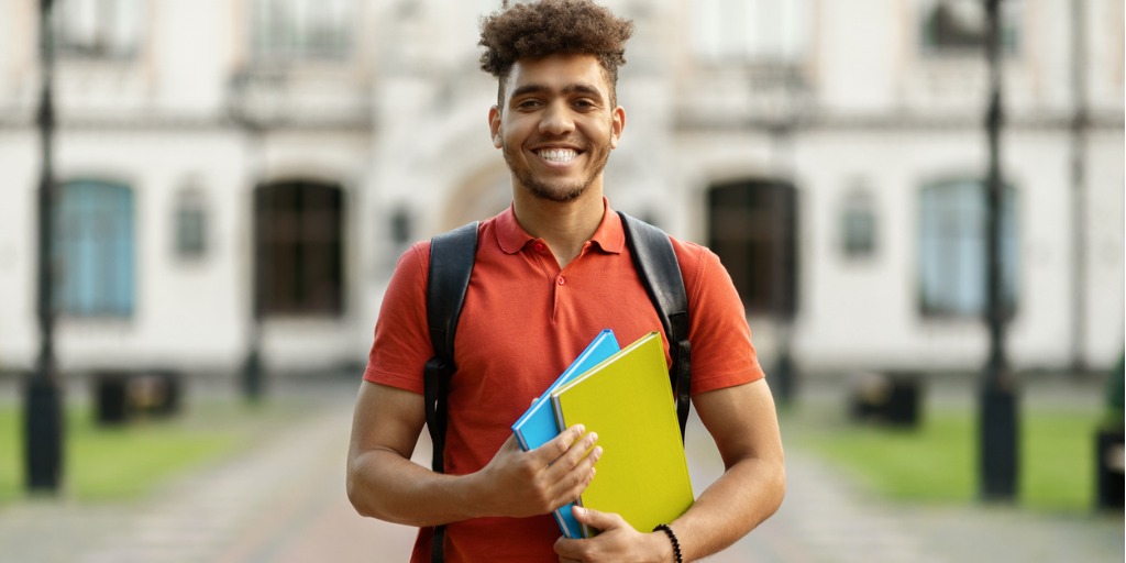 Cheerful Black Student Guy Holding Workbooks Posing Wit