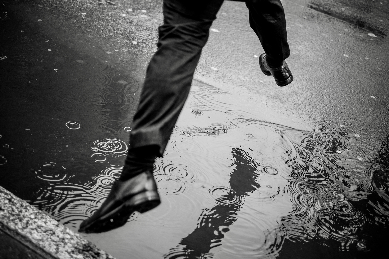 businessman jumping off a curb trying to clear a puddle