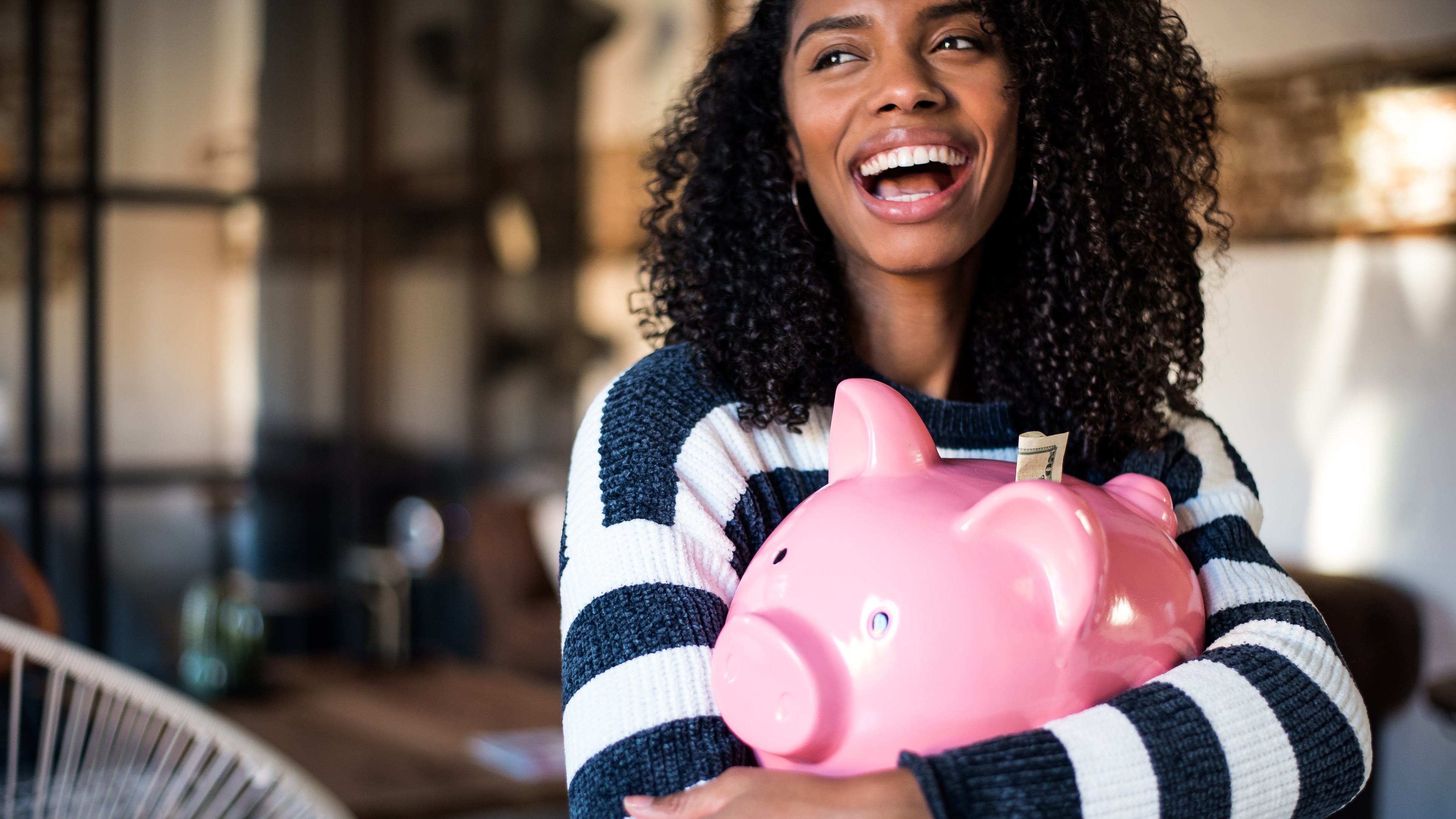 Black young woman hugging her pink piggy bank