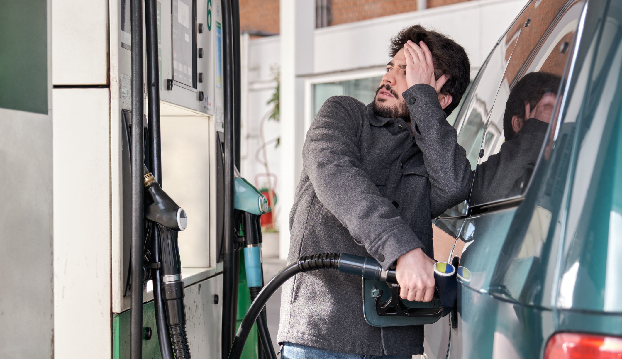 Young man refueling his vehicle while looking worried a