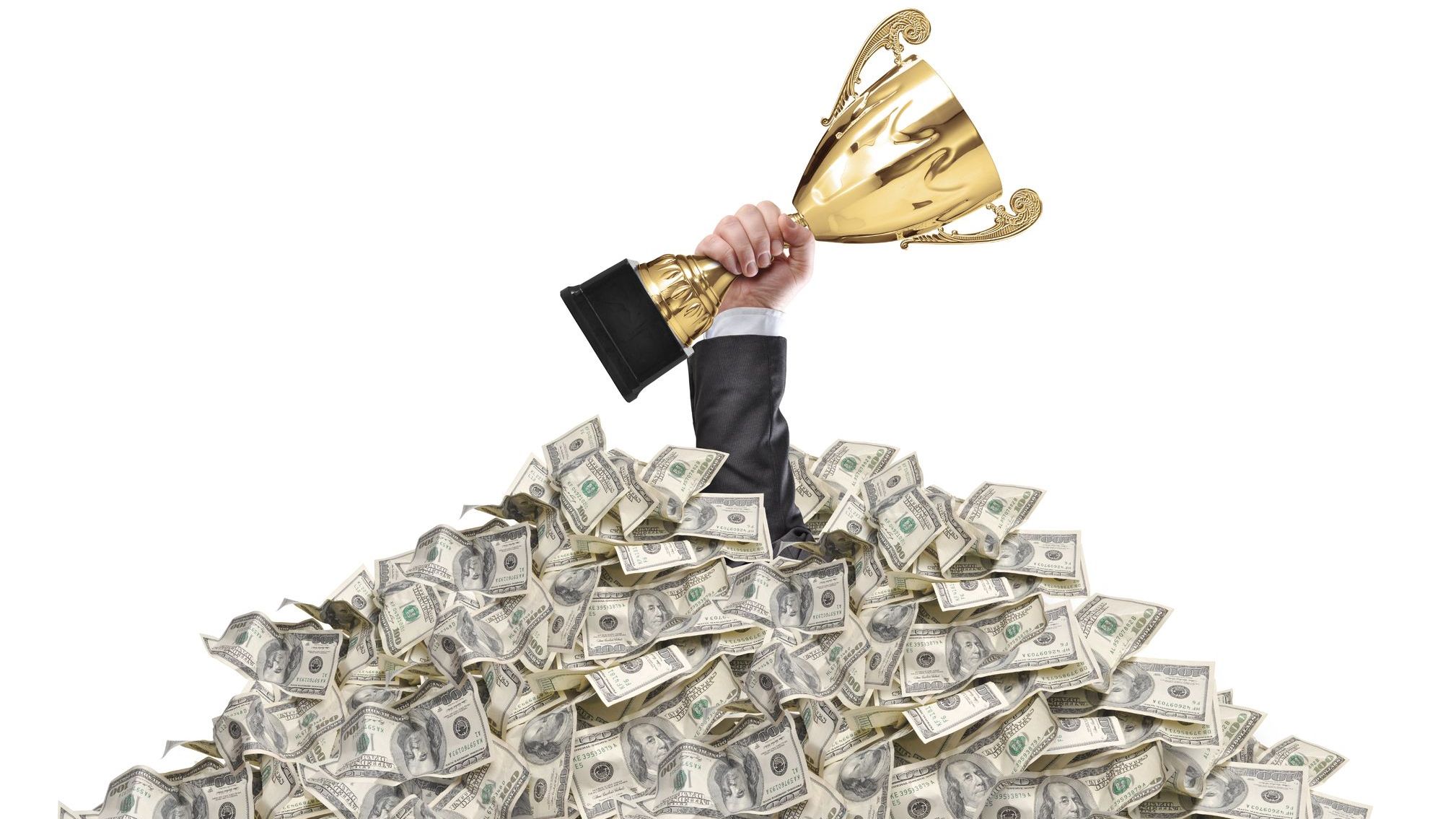 hand of a man stuck in a pile of money holding a cup trophy above the surface