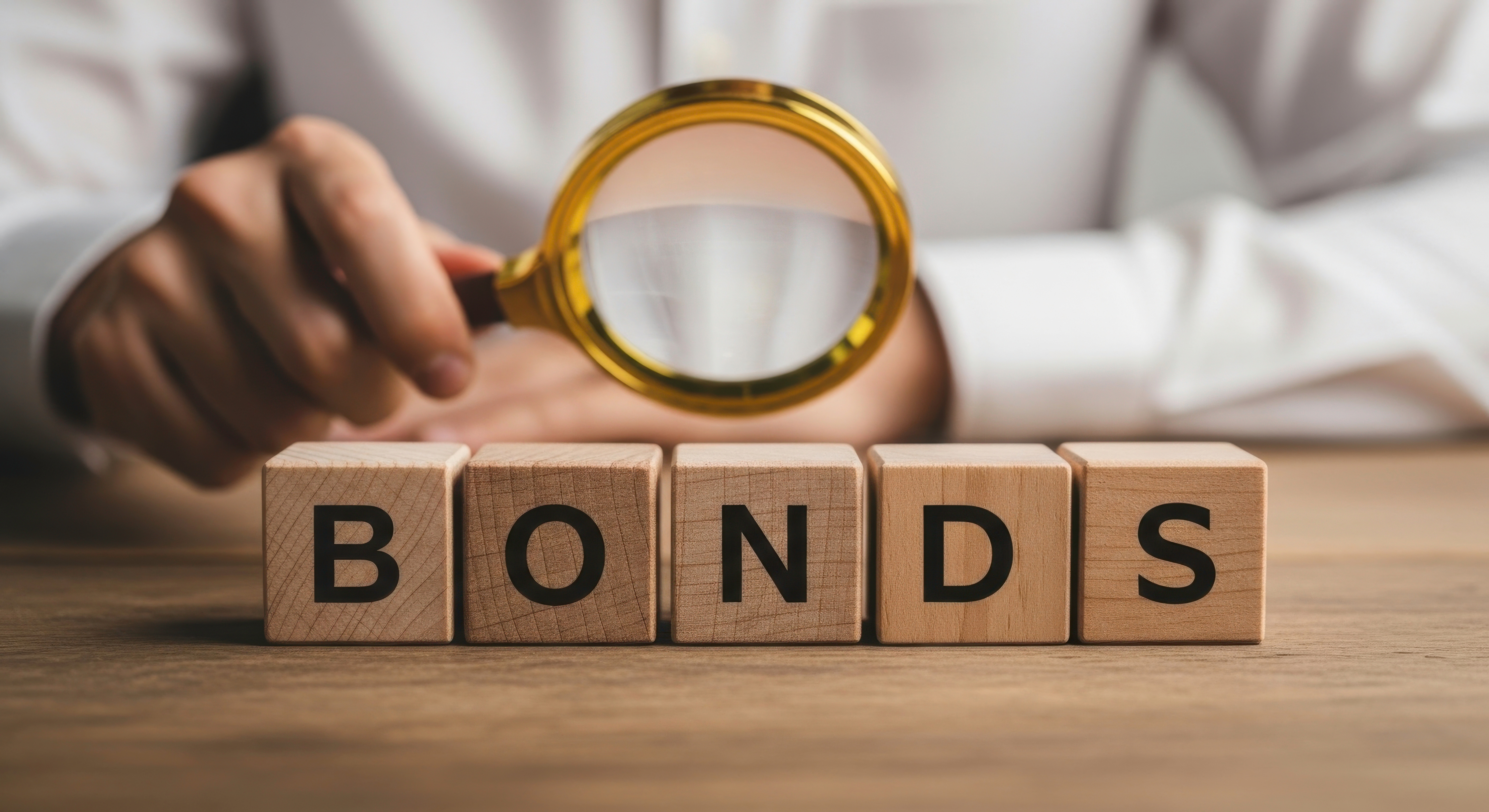 Close up of wooden blocks spelling bonds being examined with a magnifying glass held by hand 
